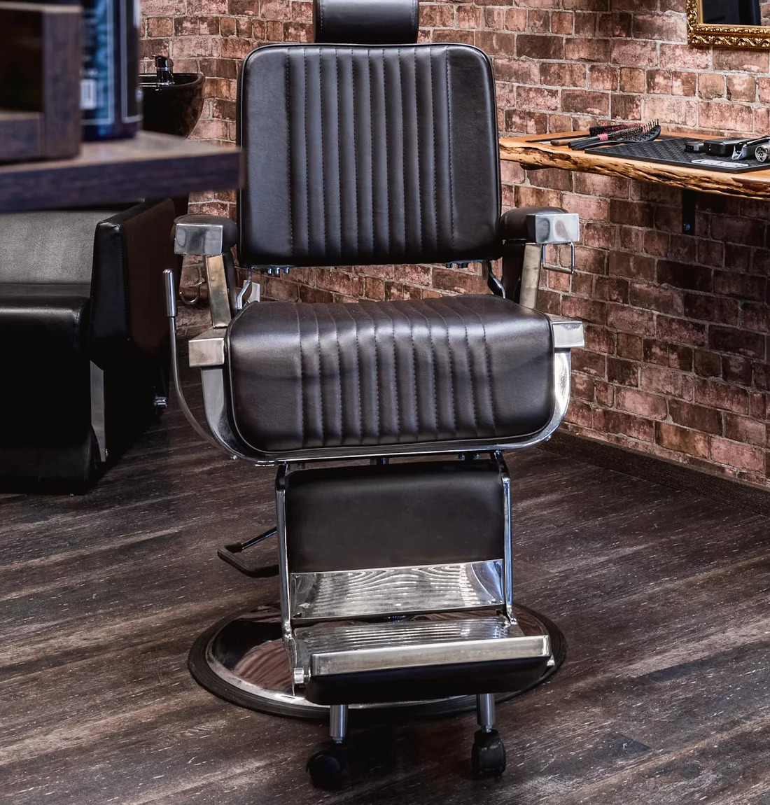 Sillón de barbero de piel negra frente a un muro de ladrillo