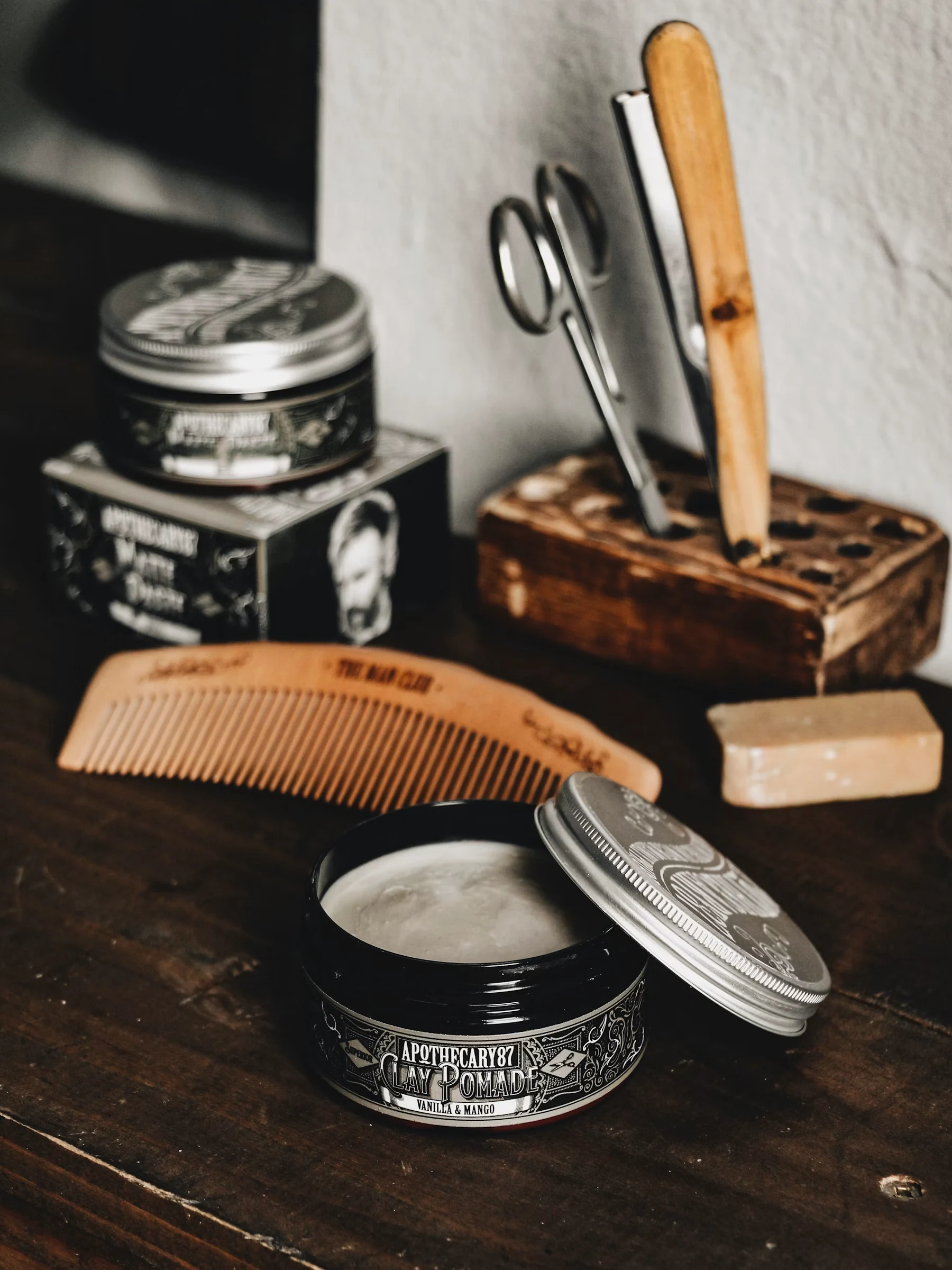 Latas de pomada, peine de madera, tijeras y jabón sobre una mesa de madera